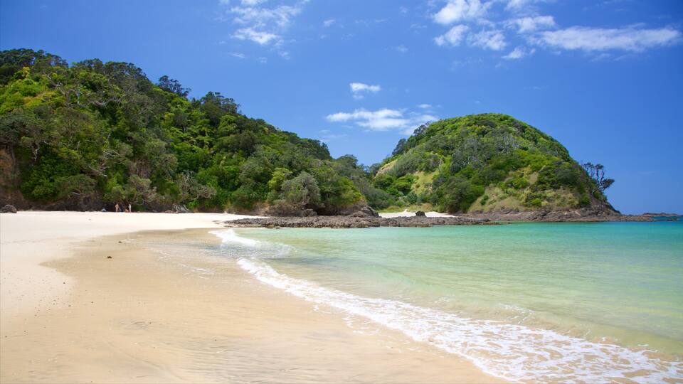 A beach with clear turquoise water, white sand, and lush green hills.