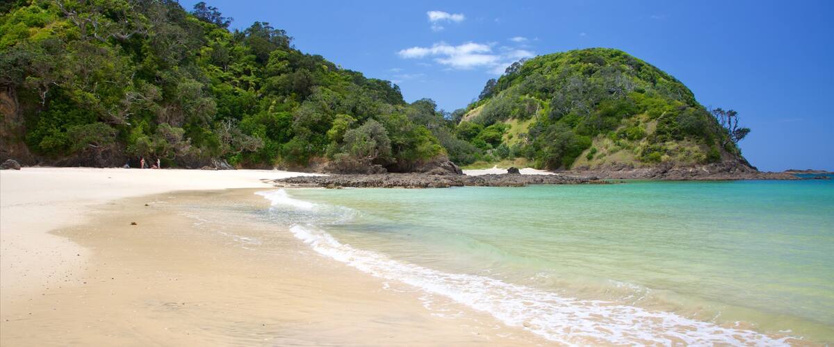 A beach with clear turquoise water, white sand, and lush green hills.