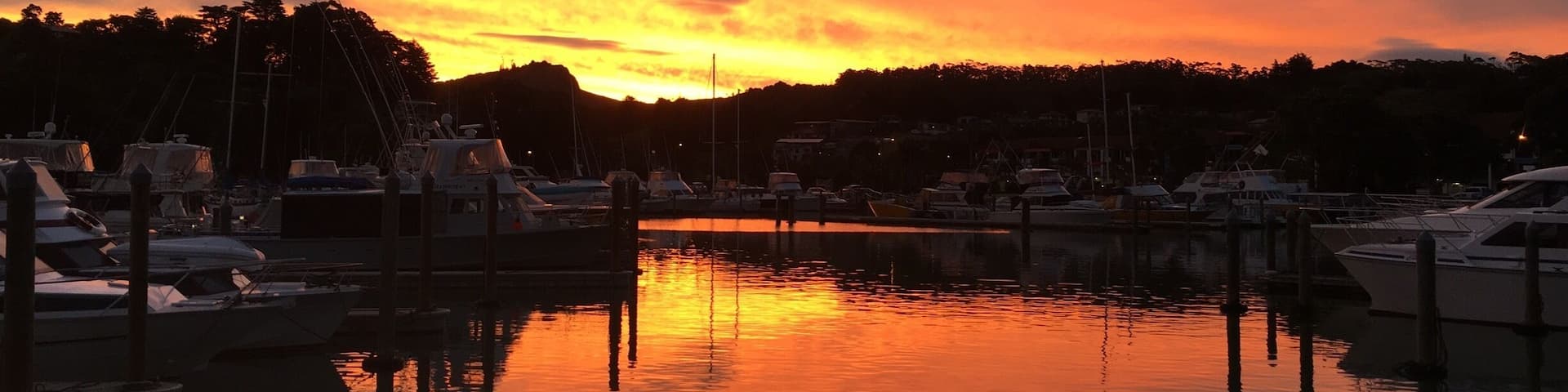 A marina at sunset with boats docked and a reflection on the water.