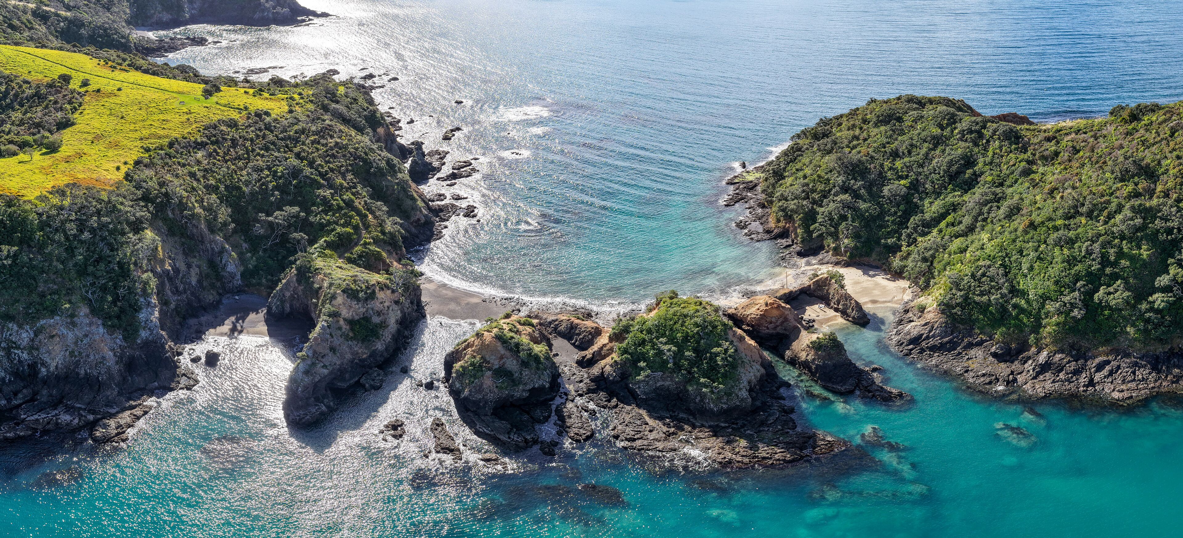 A coastal landscape with rocky cliffs, clear turquoise waters, and lush green vegetation.