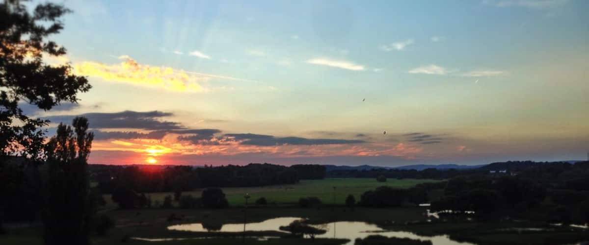 A sunset over a landscape with a pond and trees.