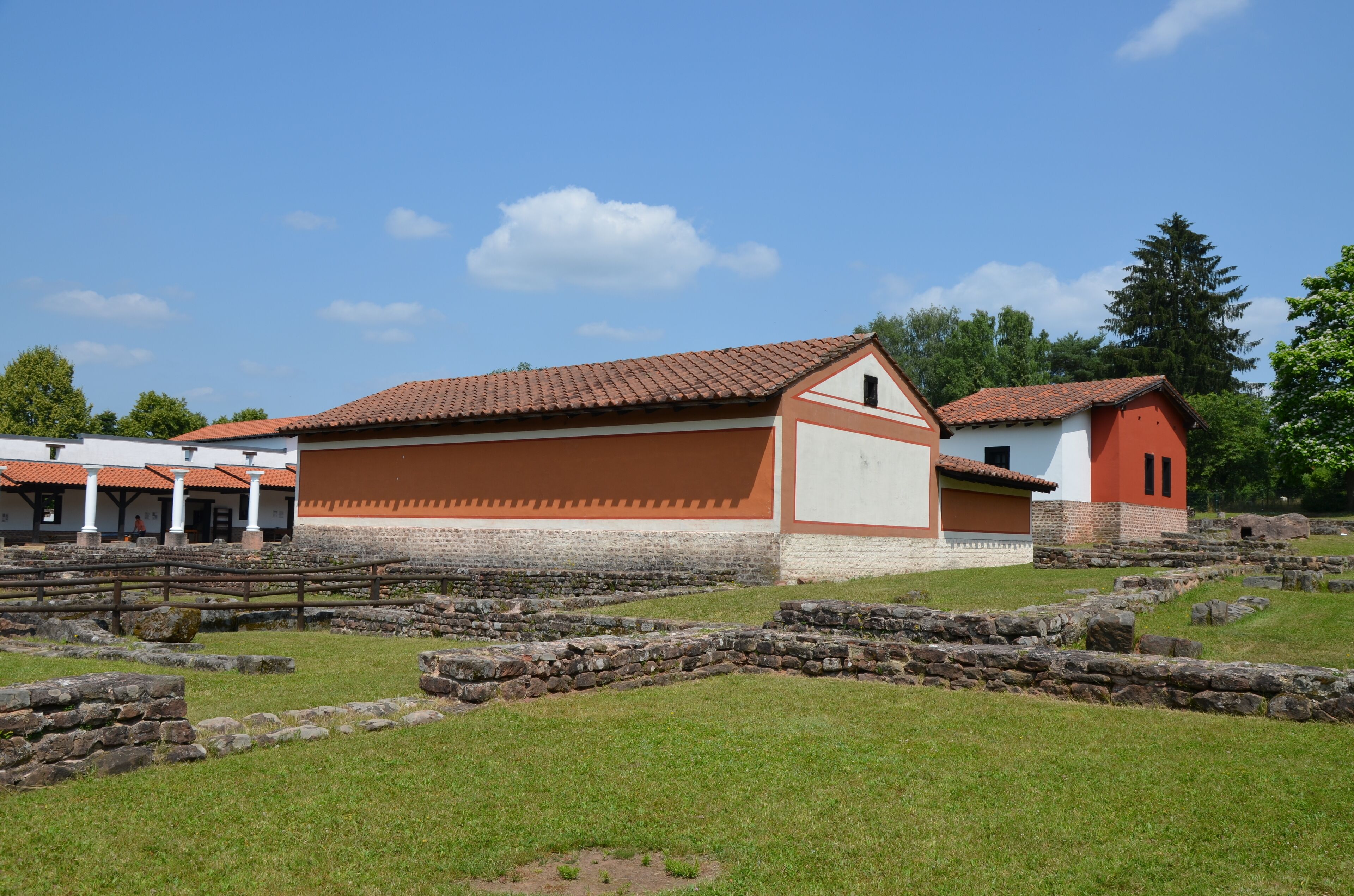 An archaeological site with ancient stone structures and a building with a red-tiled roof.