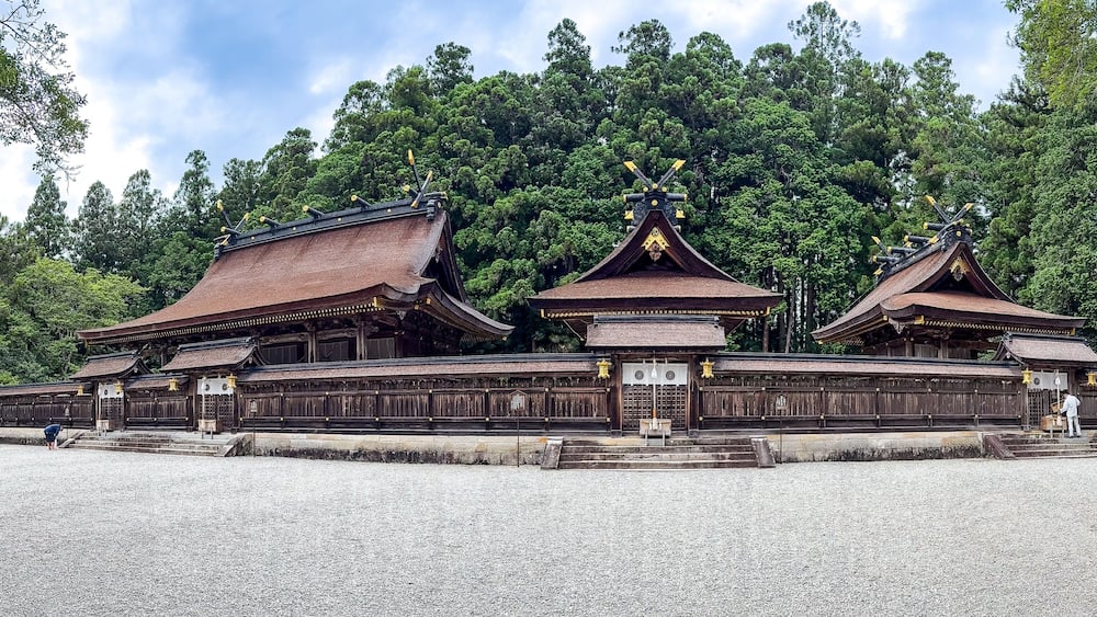 A traditional wooden structure with multiple roofs and a forested backdrop.