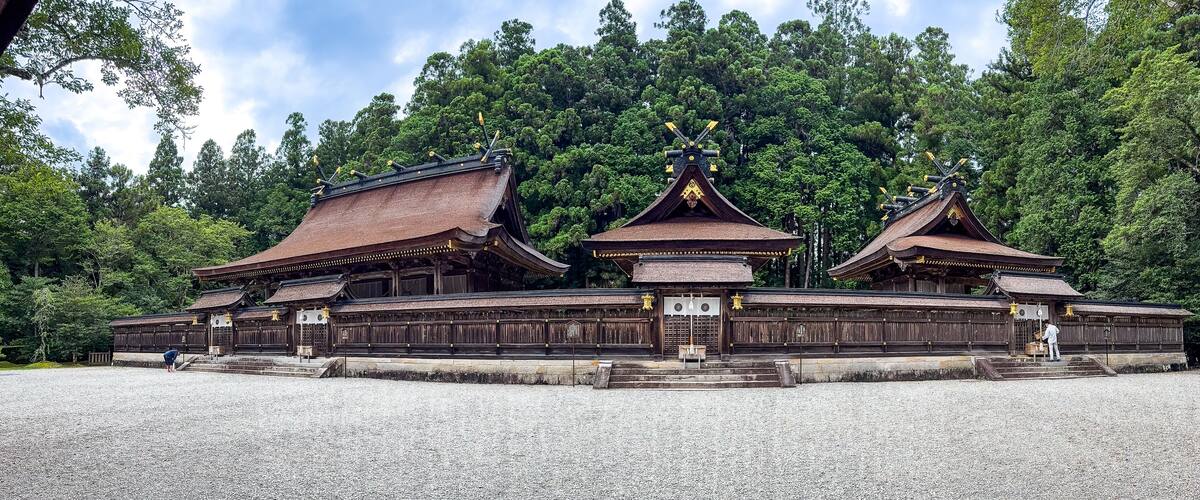 A traditional wooden structure with multiple roofs and a forested backdrop.