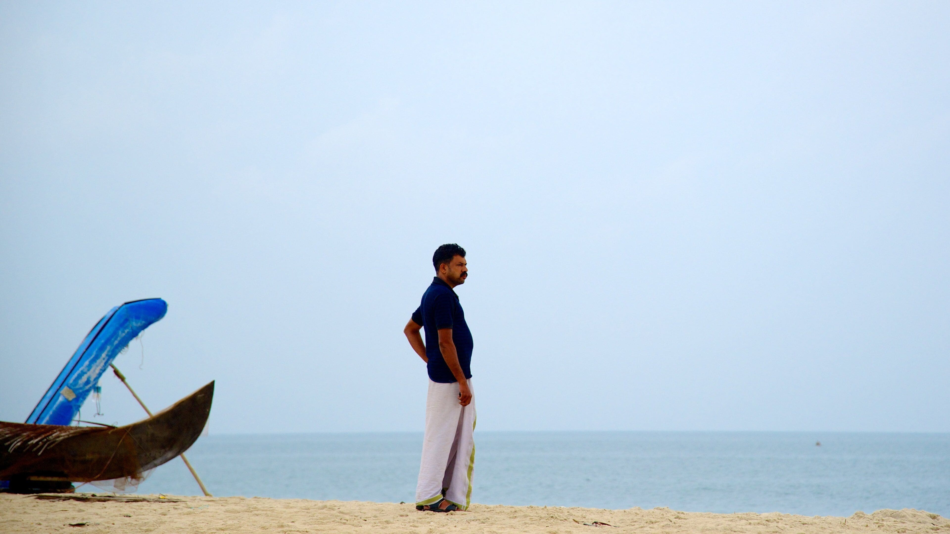 A man standing on a sandy beach with a boat in the background.