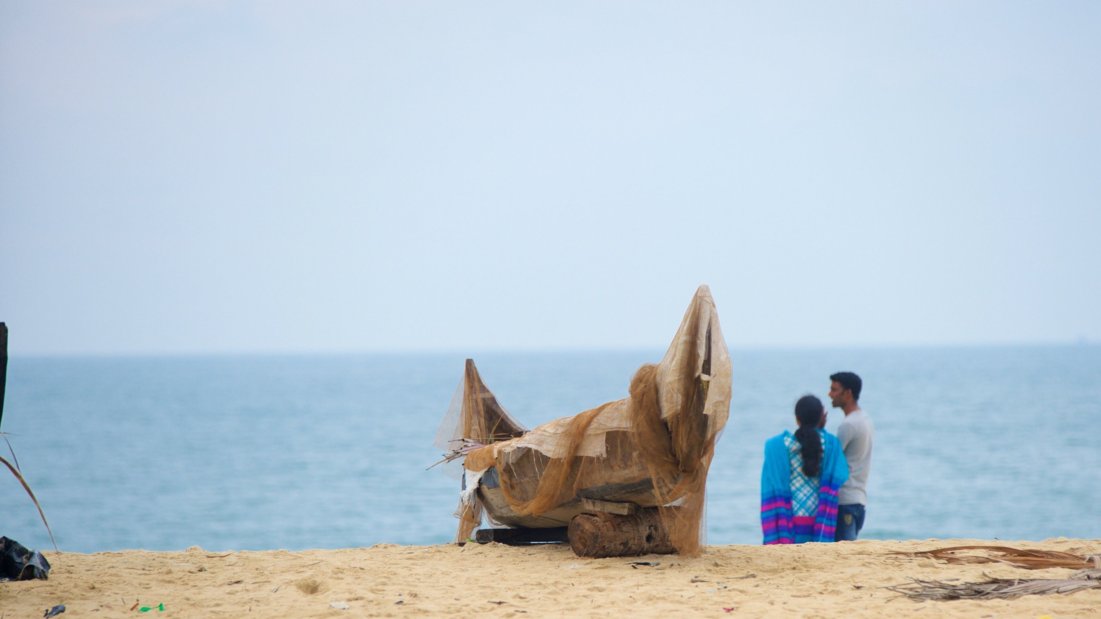 A large wooden boat on a sandy beach with the ocean in the background.