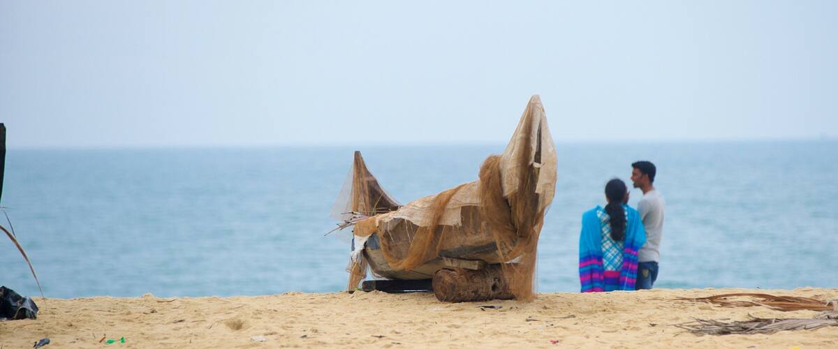 A large wooden boat on a sandy beach with the ocean in the background.
