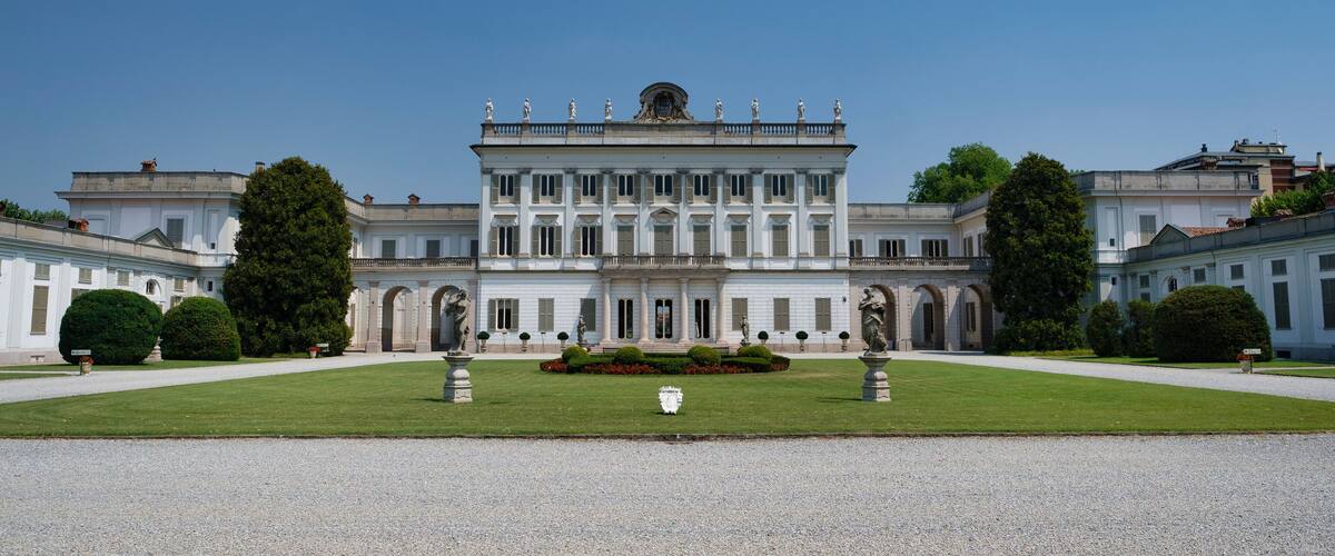 A grand classical building with symmetrical architecture, a central statue, and well-manicured gardens.