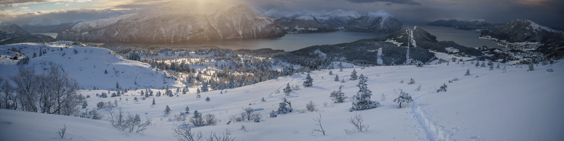 A snow-covered mountain landscape with a lake and a path leading to a cabin.