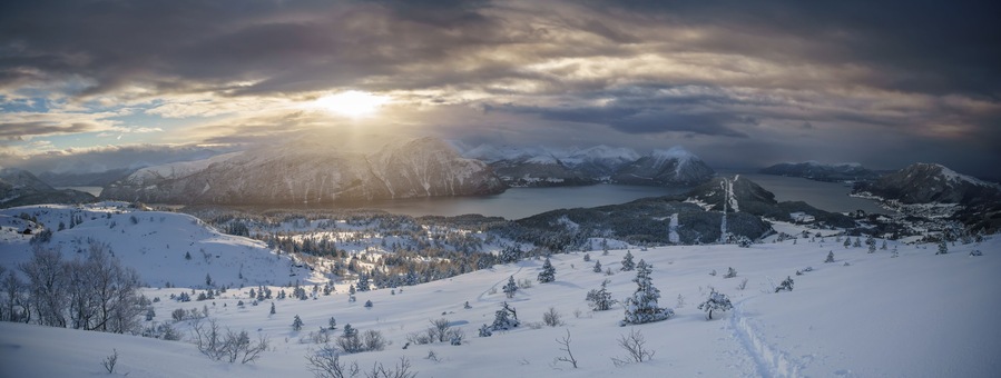 A snow-covered mountain landscape with a lake and a path leading to a cabin.