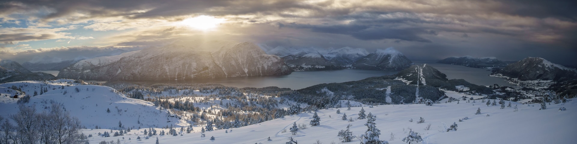 Eine verschneite Berglandschaft mit einem See und einem Weg zu einer Hütte.