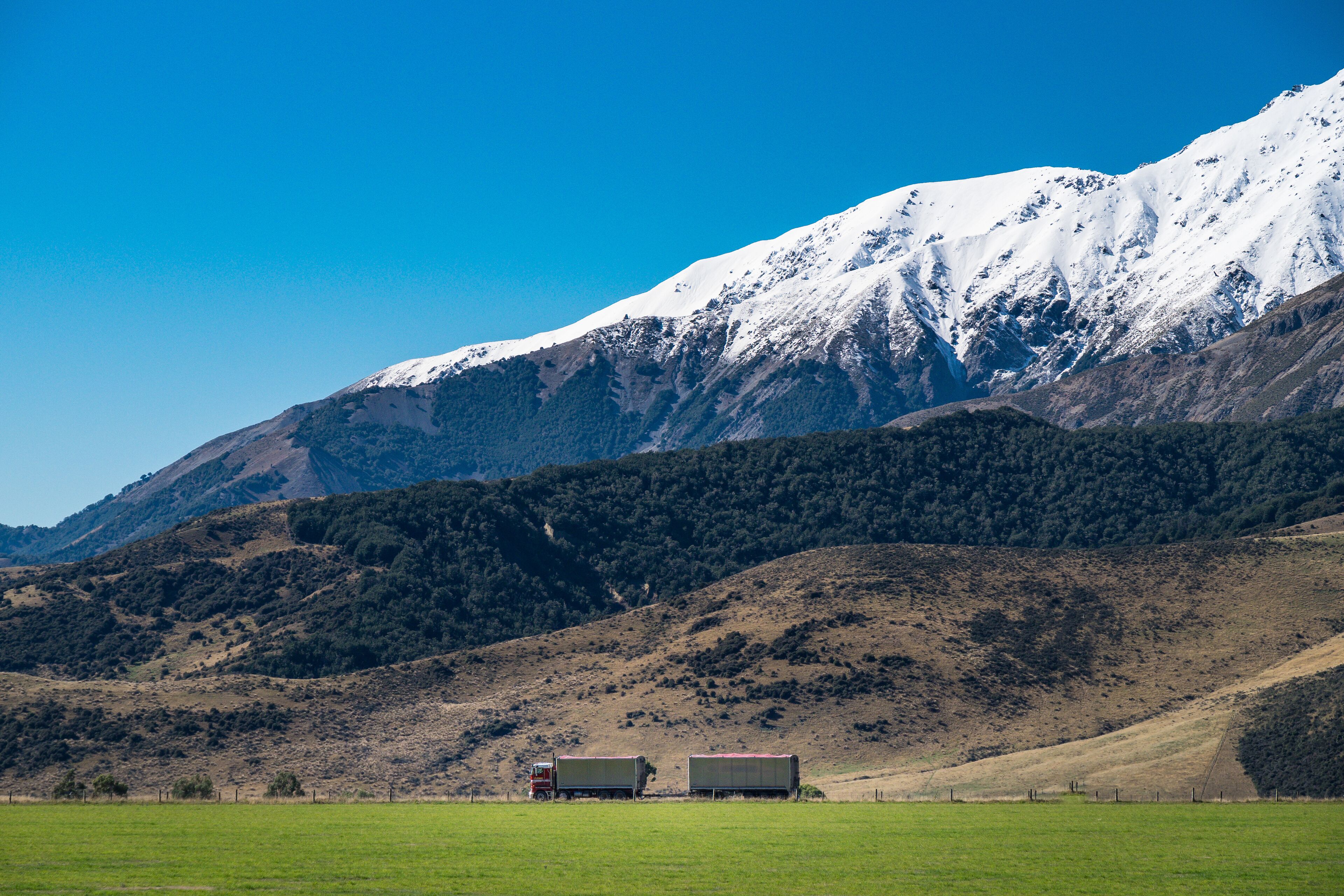 A mountainous landscape with snow-capped peaks and two trucks parked in a green field.