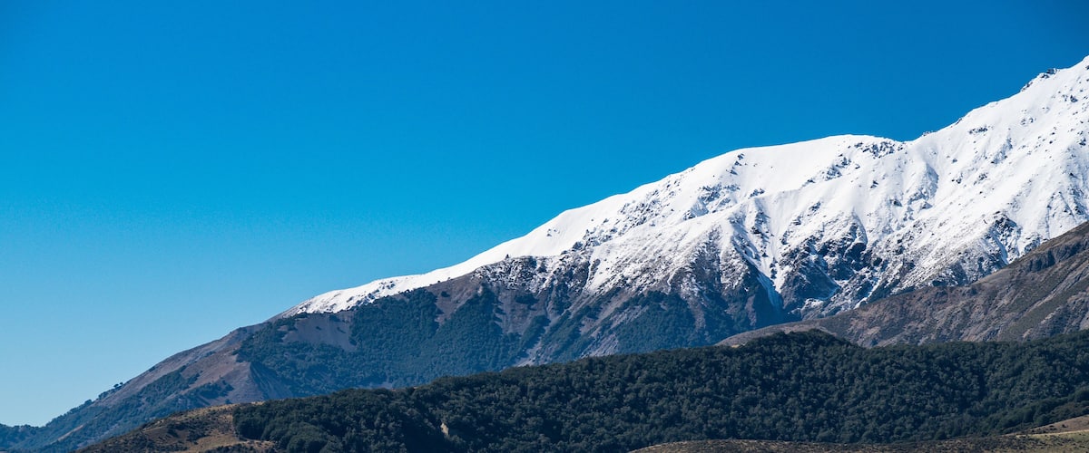 A mountainous landscape with snow-capped peaks and two trucks parked in a green field.