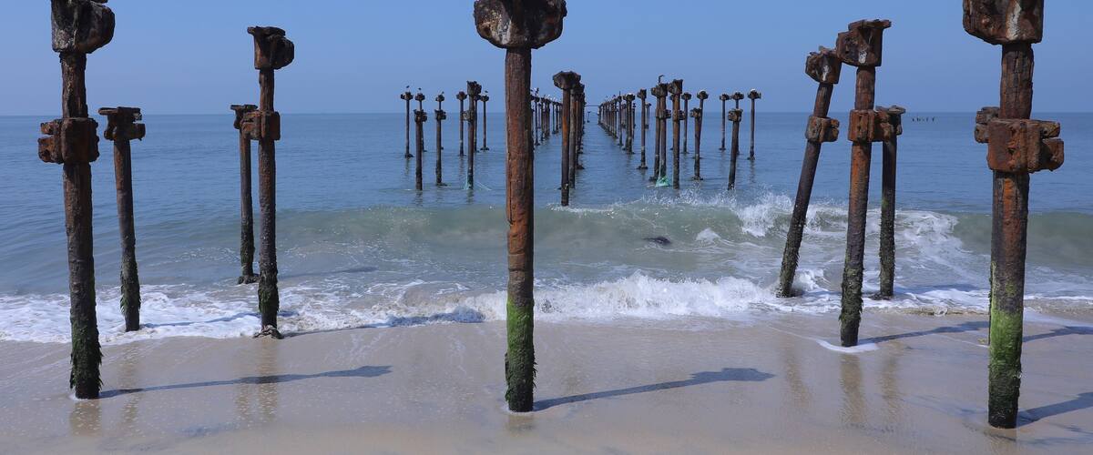 A beach with rusted metal posts and waves crashing onto the shore.