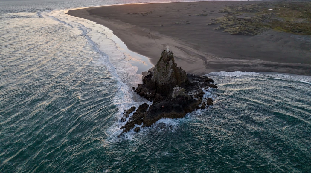 Un paysage cĂŽtier avec un affleurement rocheux au premier plan et une plage de sable qui sâĂ©tend jusquâĂ lâocĂ©an.