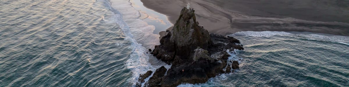 A coastal landscape with a rocky outcrop in the foreground and a sandy beach extending to the ocean.