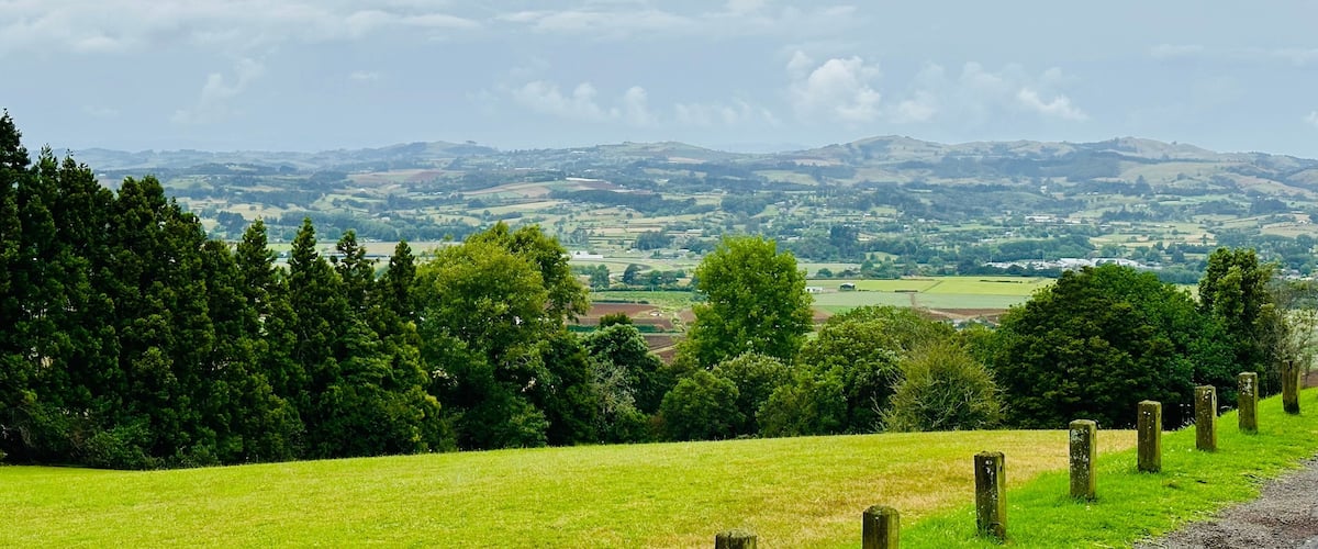 A lush green field with a distant view of rolling hills and a cloudy sky.