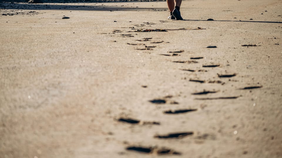 A sandy beach with footprints leading towards the water.