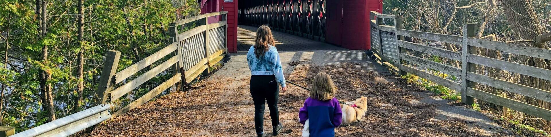 A mother and daughter walking together through the red Wakefield covered bridge along the Gatineau River on a beautiful sunny fall day in pretty town of Wakefield, Quebec, Canada.