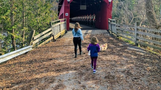 A mother and daughter walking together through the red Wakefield covered bridge along the Gatineau River on a beautiful sunny fall day in pretty town of Wakefield, Quebec, Canada.