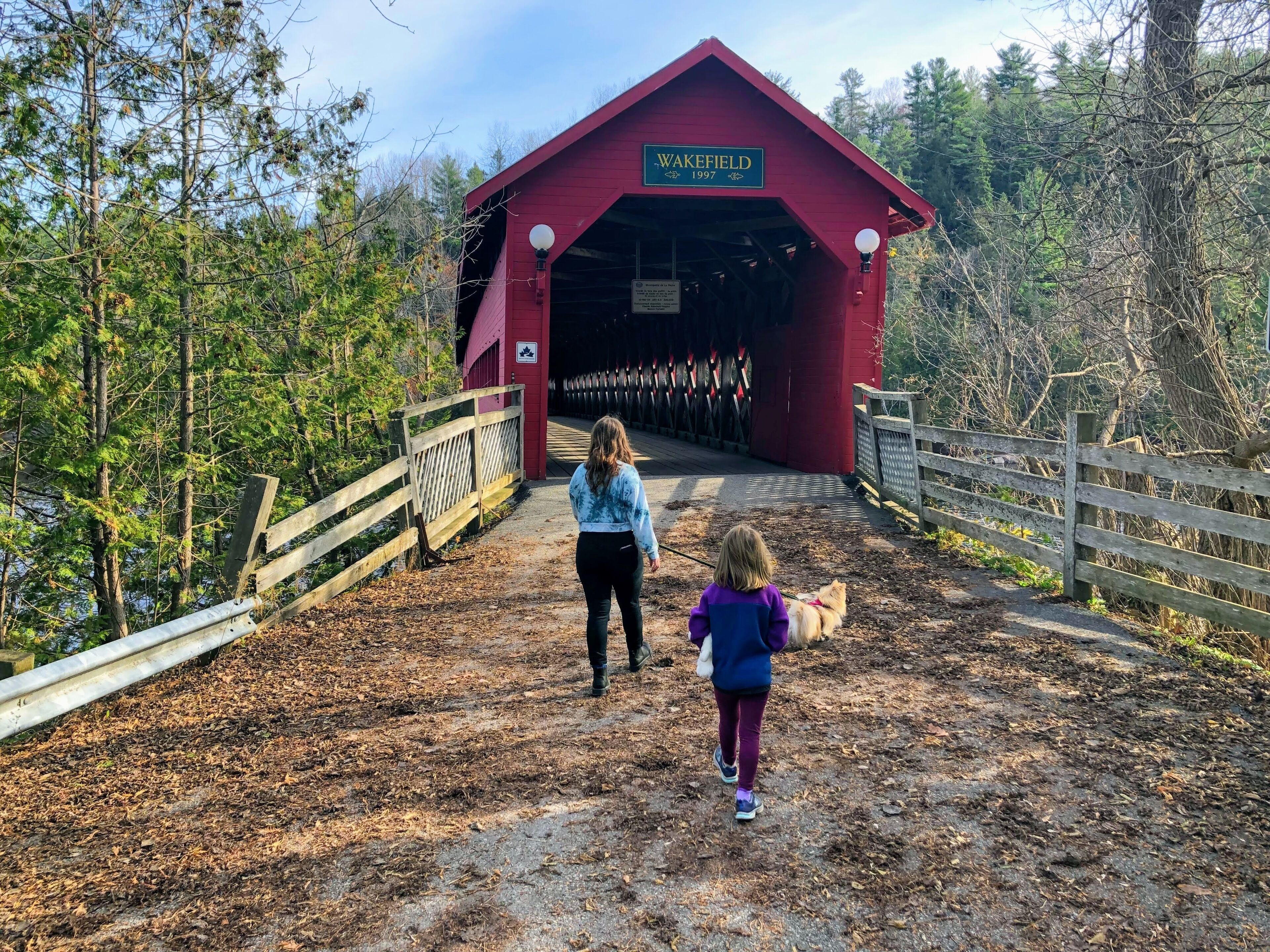 A red covered bridge labeled 'Wakefield 1997' with a woman and a child walking towards it.