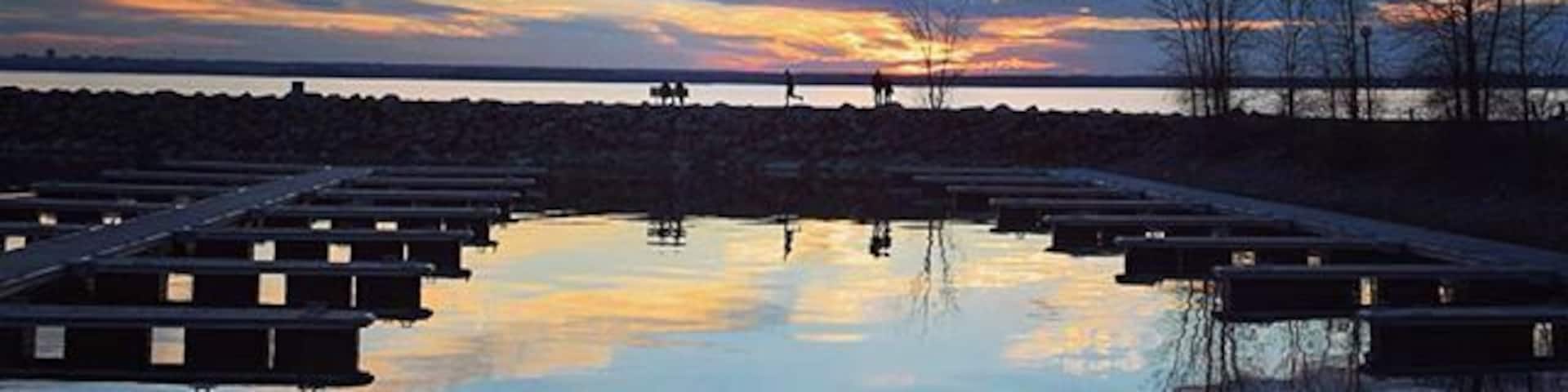 A sunset over a calm body of water with dock structures and leafless trees.