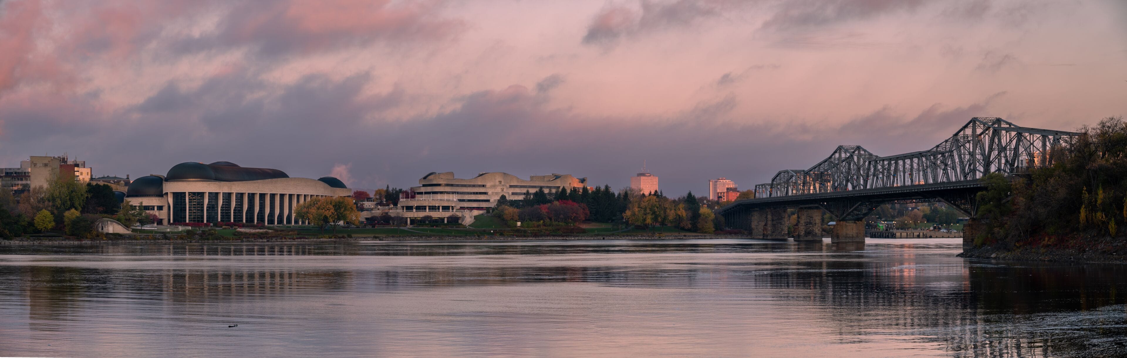 A river with a bridge, a large building with a dome, and a city skyline in the background.