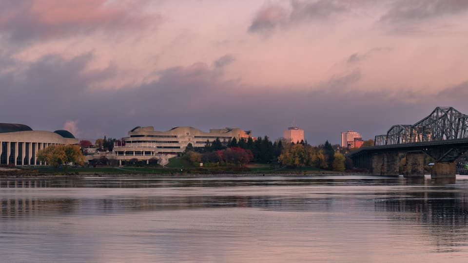 A river with a bridge, a large building with a dome, and a city skyline in the background.