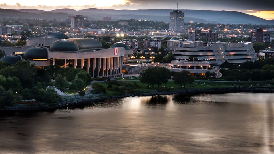 A cityscape with a river, modern architecture, and a mountainous backdrop.