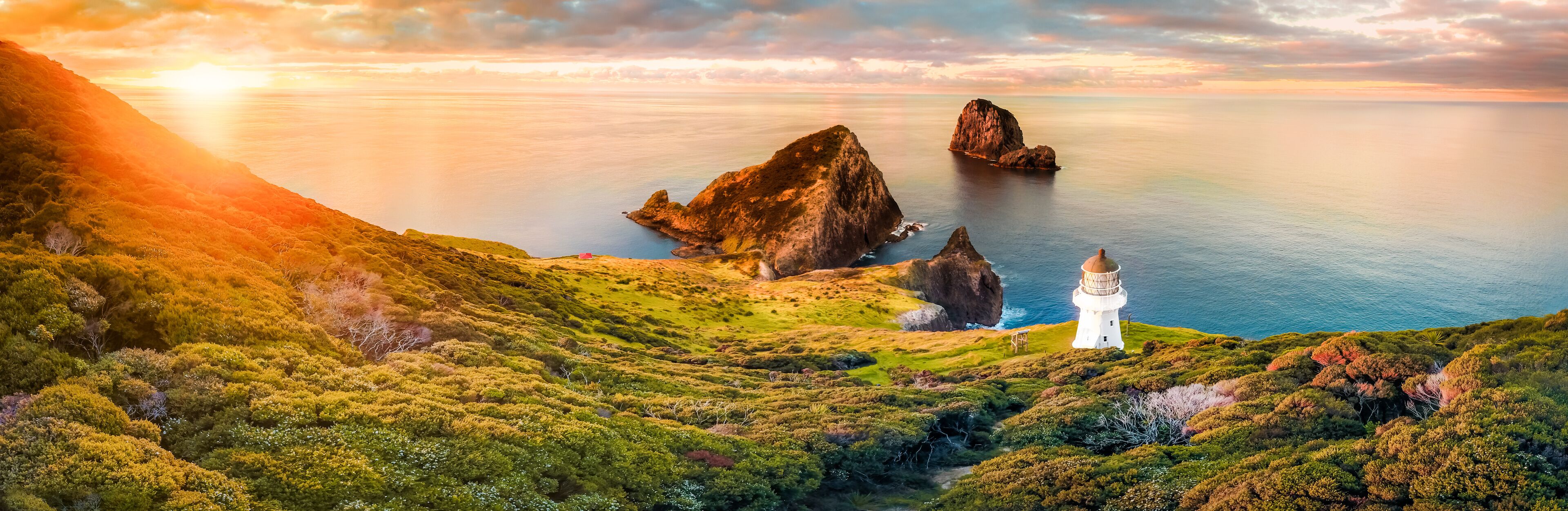 A coastal landscape with a lighthouse, rocky cliffs, and lush greenery.