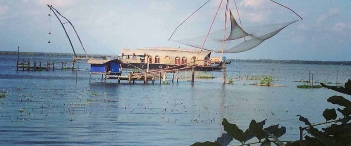 A traditional boat with a large net on a calm body of water, surrounded by vegetation.