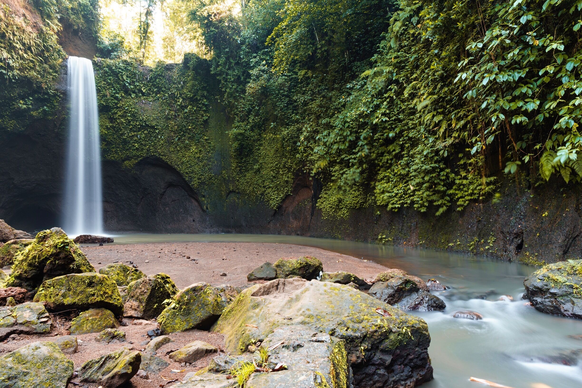 A waterfall cascading into a river surrounded by moss-covered rocks and dense greenery.