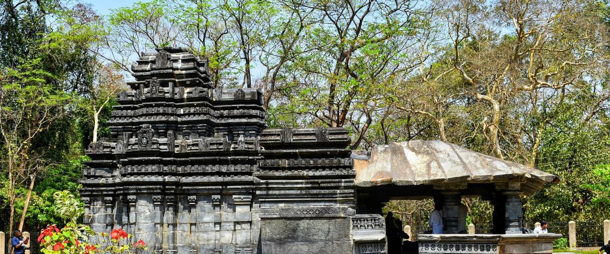 A temple with intricate carvings and a stone pavilion in a landscaped garden.