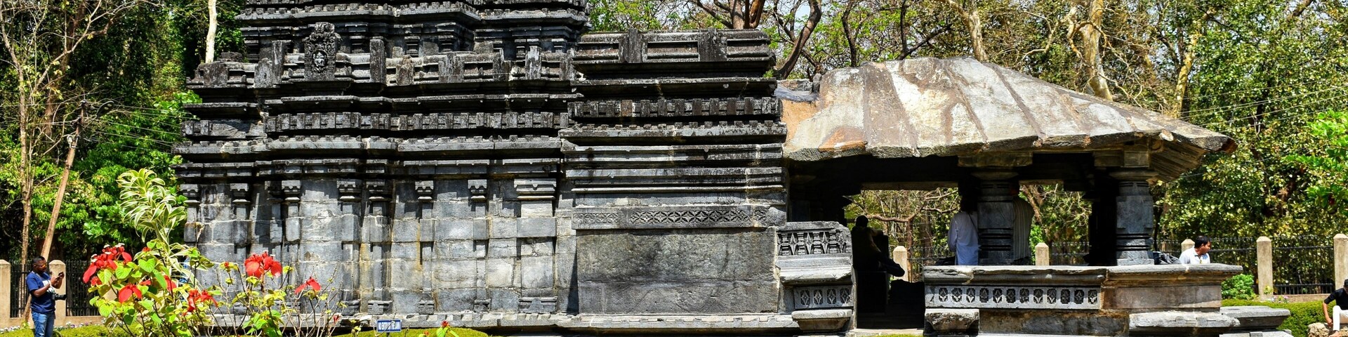 A temple with intricate carvings and a stone pavilion in a landscaped garden.