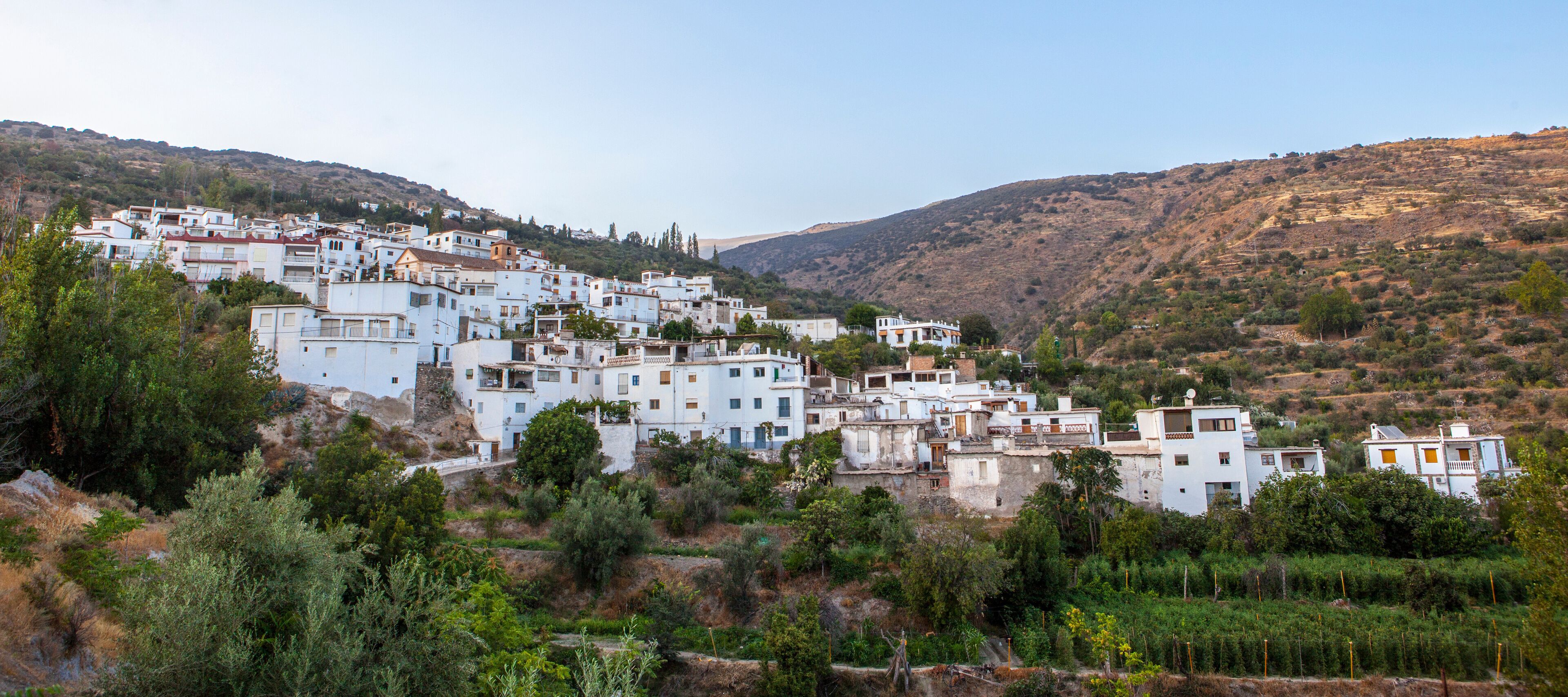 A white-washed village nestled in a hilly landscape with dense greenery and rocky terrain.