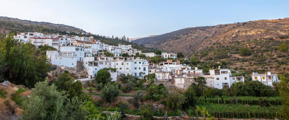 A white-washed village nestled in a hilly landscape with dense greenery and rocky terrain.