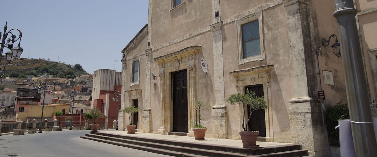 A historic building with a weathered facade, a prominent entrance, and potted plants at the base.