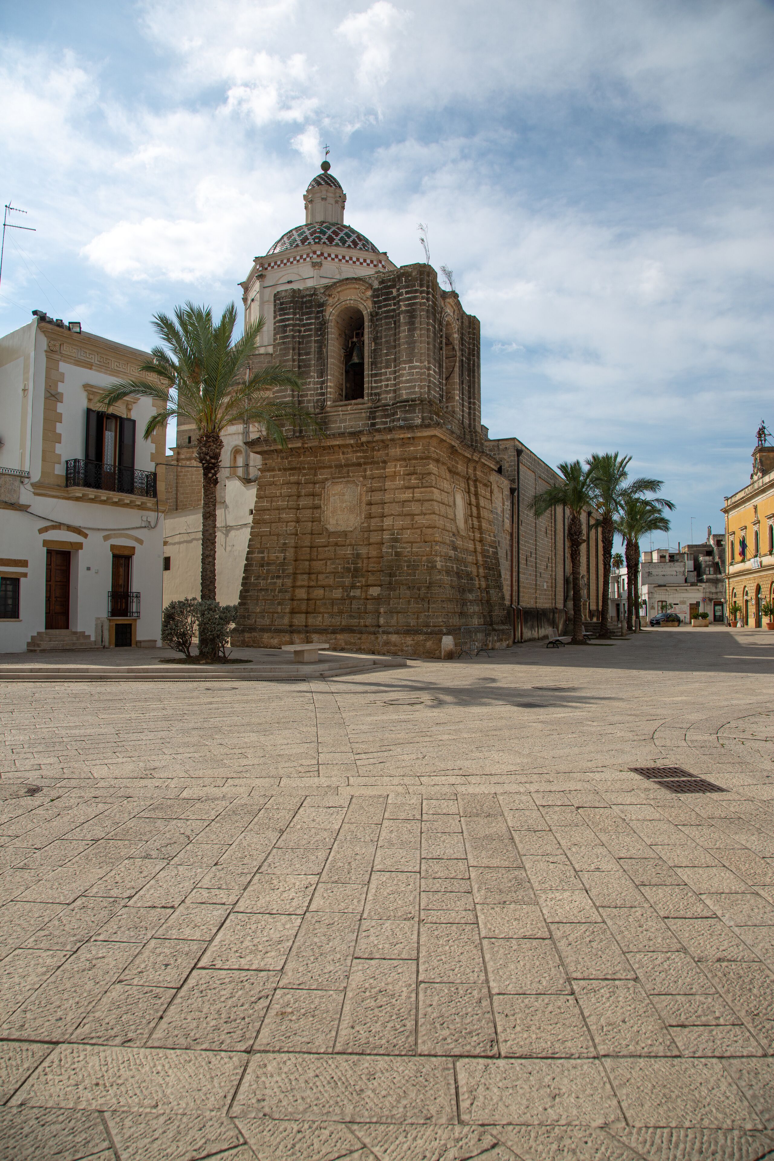 A historic plaza with a prominent church featuring a dome and bell tower, palm trees, and traditional buildings.