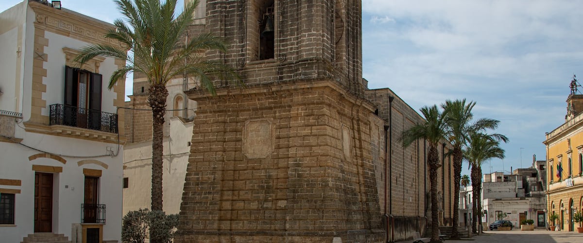 A historic plaza with a prominent church featuring a dome and bell tower, palm trees, and traditional buildings.
