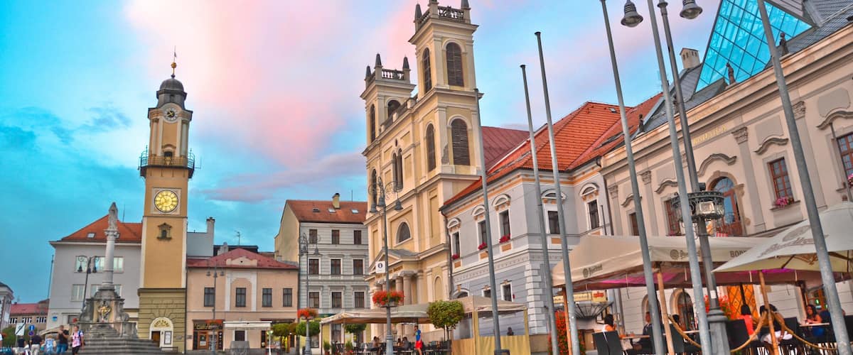 A historic square with a clock tower, a church, and outdoor cafes.