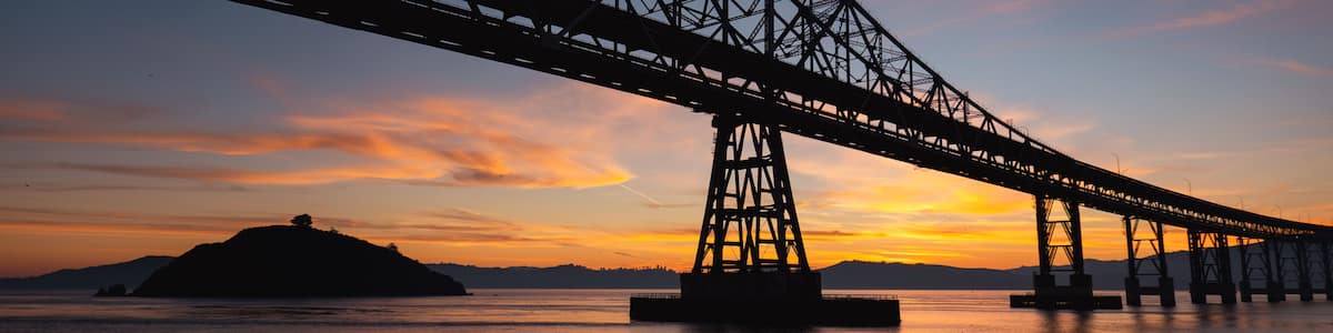 A bridge spanning a body of water with a sunset in the background.