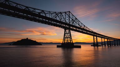 Uma ponte sobre a água, com o pôr do sol ao fundo.