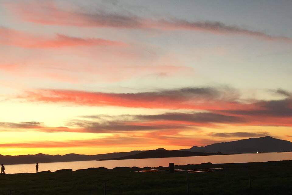 Un capvespre sobre una massa d'aigua, amb siluetes de persones i una muntanya llunyana.