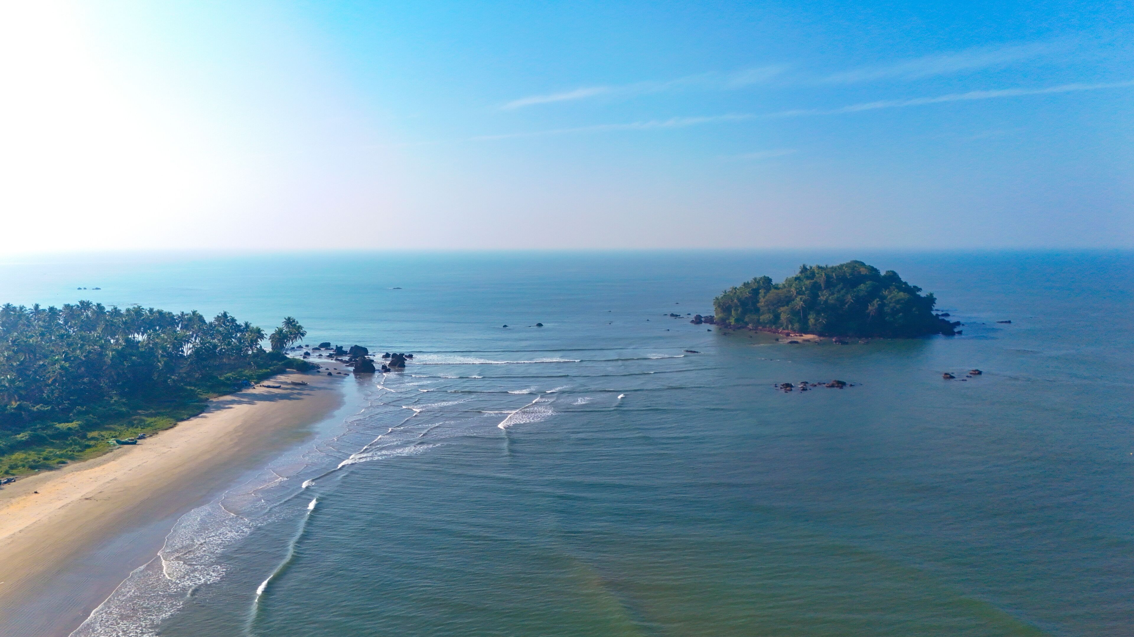 A beach with a small island surrounded by calm waters.
