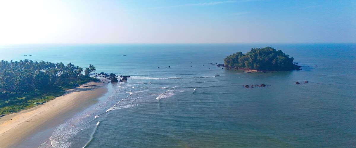 A beach with a small island surrounded by calm waters.