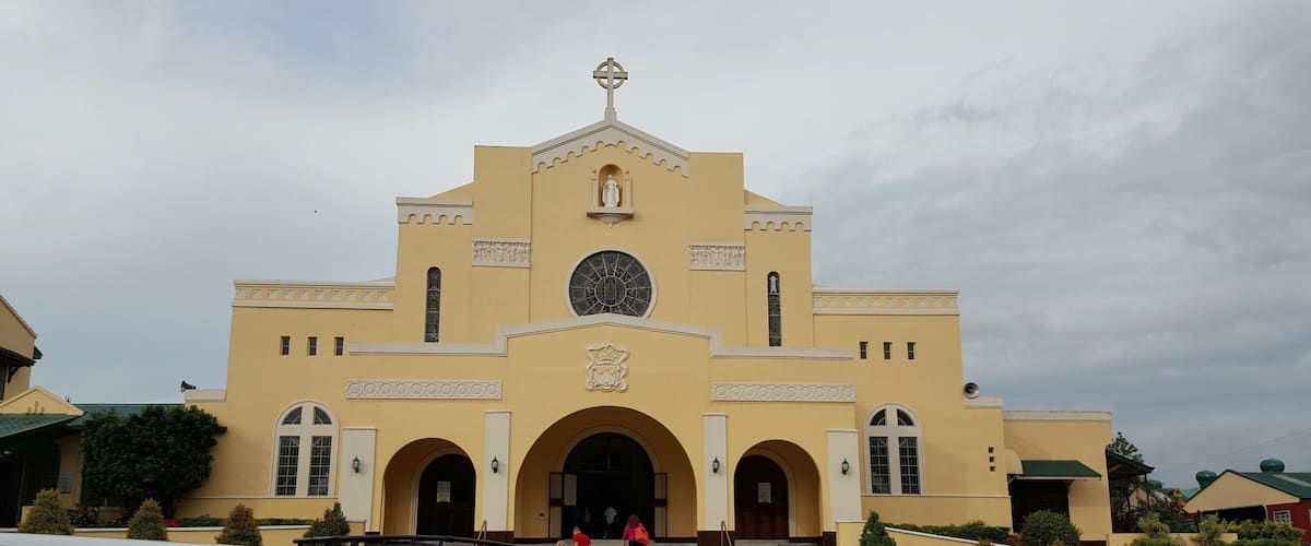A yellow church with a large circular window, arched entrances, and a cross on top.