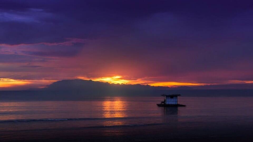 A sunset over a calm sea with a small boat in the foreground.