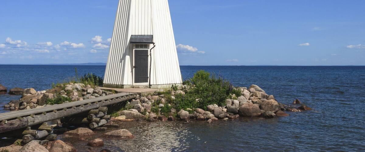 A white lighthouse on a rocky shore with a wooden walkway leading to it.