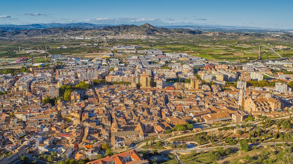 An aerial view of a city with a prominent church, surrounded by residential and commercial buildings, with mountains in the background.