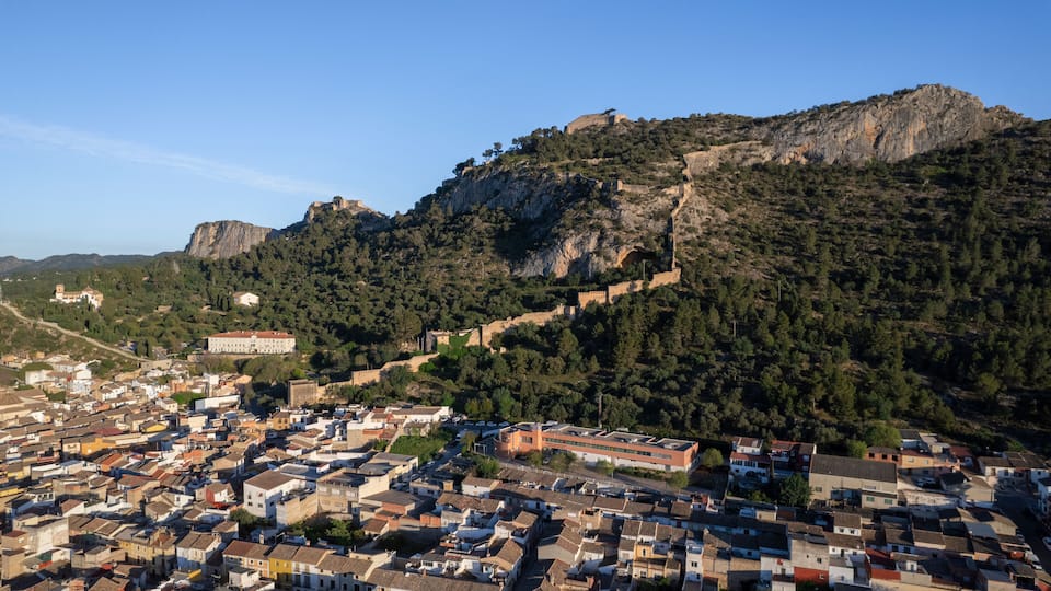 A town nestled at the base of a rocky hill with a prominent castle on top.